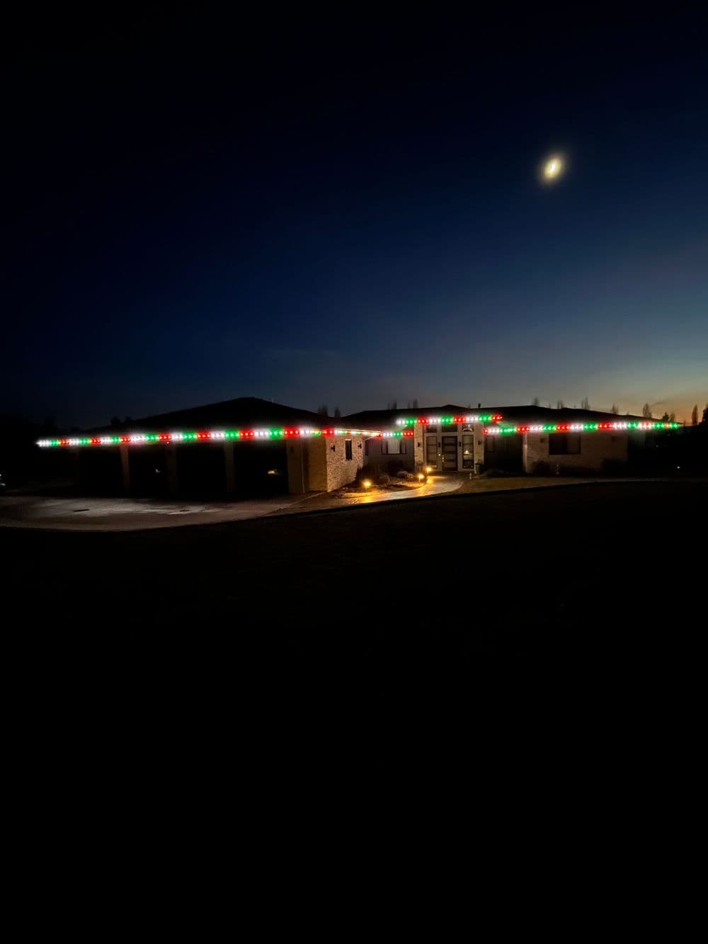 House decorated with red and green lights at night under a crescent moon.