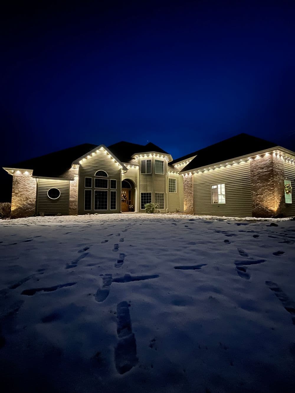 Home decorated with warm lights during winter, surrounded by snow at night.