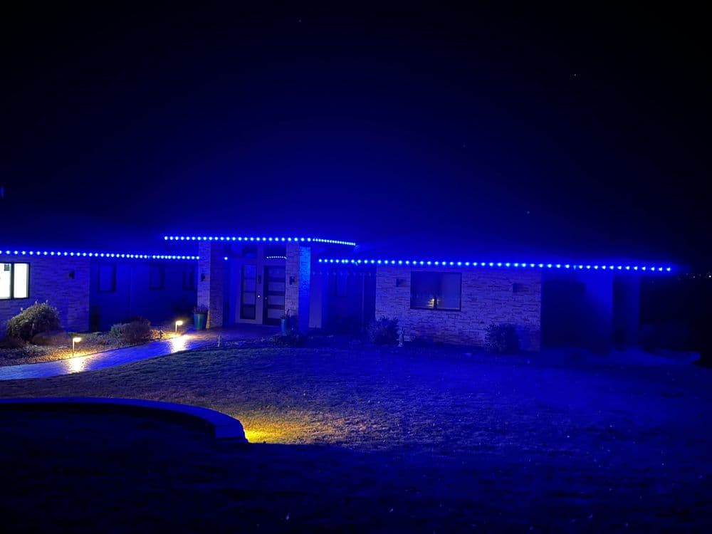 Home illuminated with blue LED lights at night, showcasing modern architectural design.